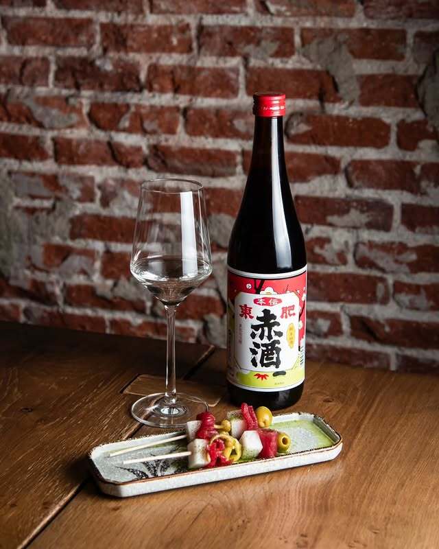 Botella de akazake japonés junto a una copa de vino y una tabla de otsumami