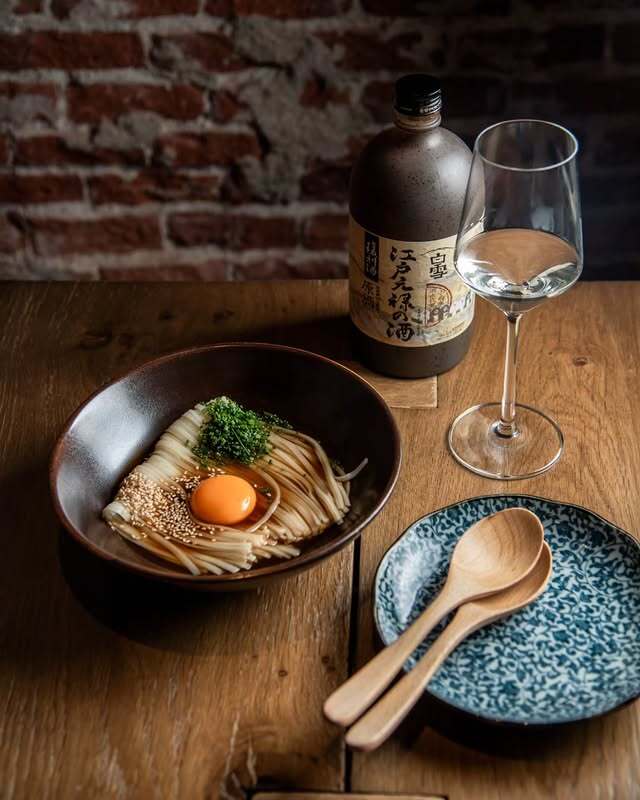 Bowl de udon frío con yema de huevo, junto a botella de sake y copa de vino